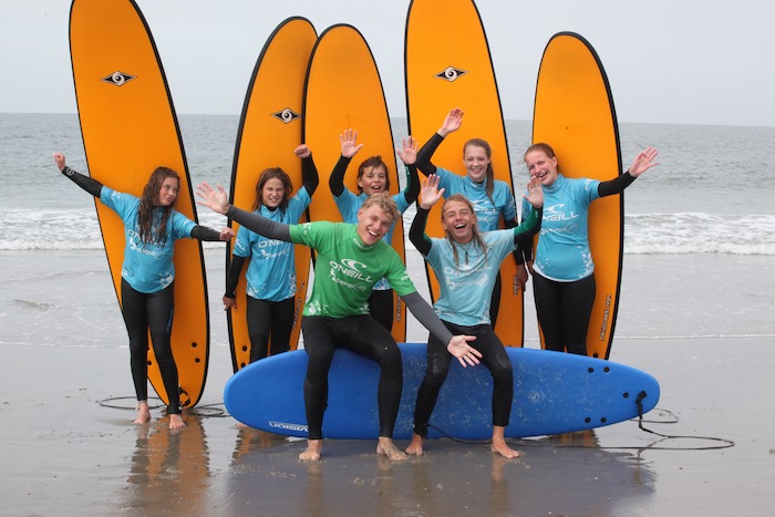 Groep jongeren poseren lachend met surfboards.