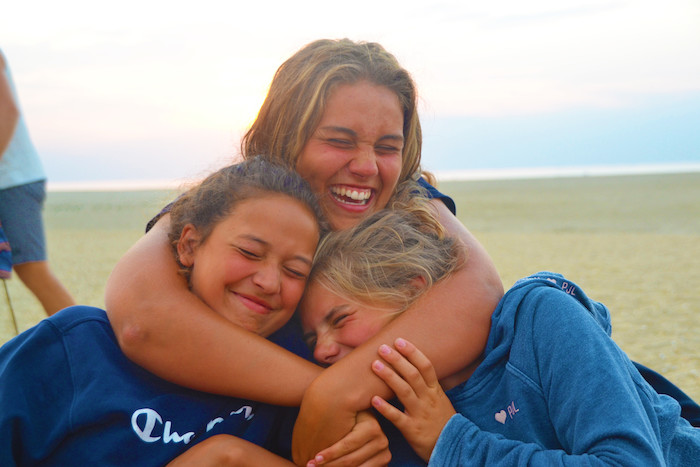 Meisjes knuffelen lachend tijdens zomerkamp in Spanje.