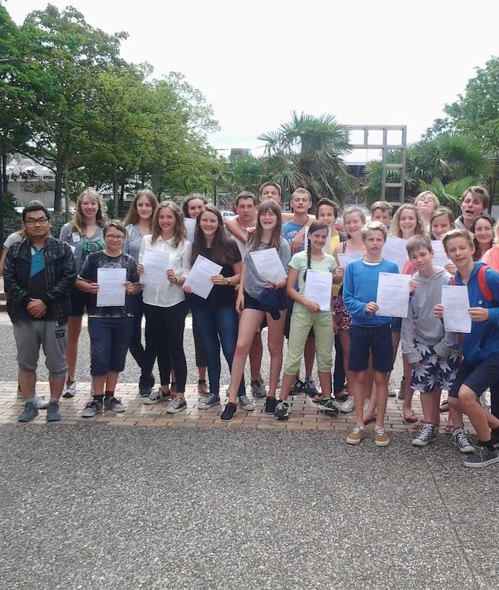 Groep poseert lachend met papieren op taalreis Frankrijk.