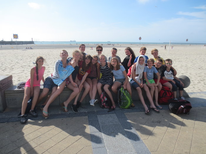 Groep tienermeisjes poseert lachend aan het strand op taalreis Frankrijk.