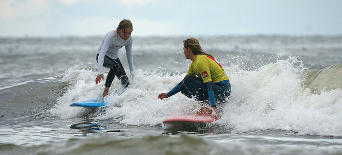 Twee tienermeisjes surfen over de golven.