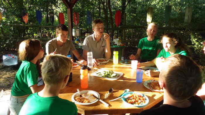 Begeleiders en jongens eten aan tafel op viskamp. 