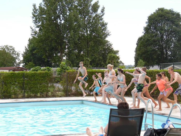 Kinder eines internationalen Feriencamps springen in den Pool