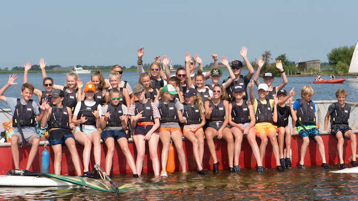 Groep lacht naar de camera op windsurfkamp.