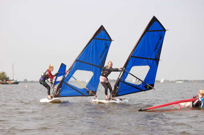 Twee tienermeisjes op windsurfkamp met blauwe zeilen.
