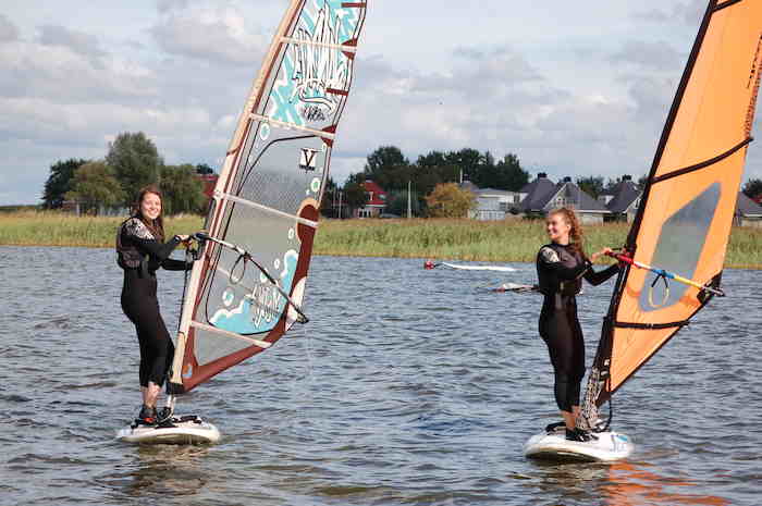 Twee meisjes windsurfen en lachen op windsurfkamp.
