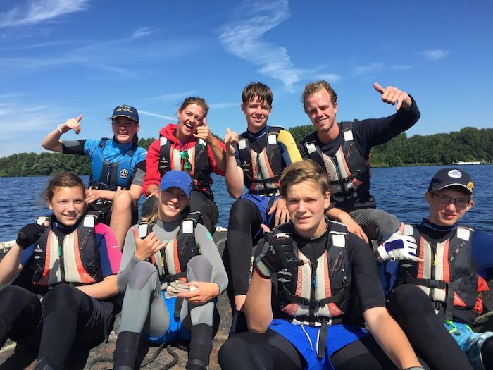 Teens in wetsuits en reddingsvesten poseren bij het meer. 