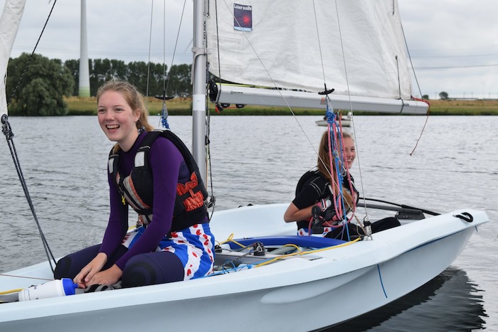 Tienermeisjes zitten lachend in zeilboot op zeilkamp. 