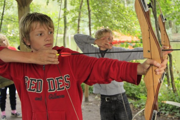 Junge zielt mit einem Bogen im Feriencamp in den Niederlanden