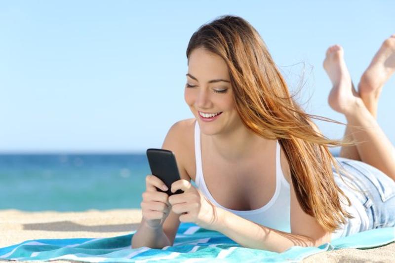 Ein Mädchen liegt während ihrer Jugendreise Italien am Strand und schaut aufs Handy
