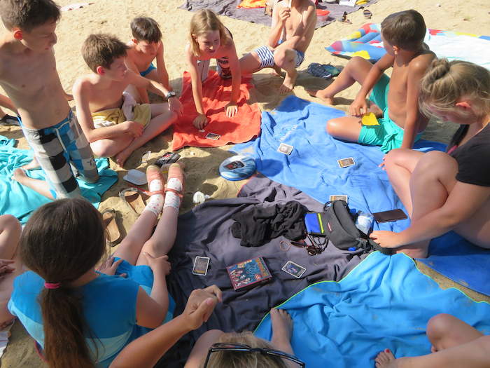Kinder eines günstigen Ferienlagers sitzen am Strand und spielen Karten.