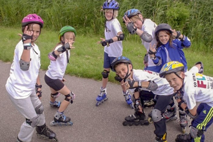 Kinderen met rolschaatsen poseren lachend op zomerkamp Amsterdam.