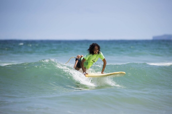 Meisje in fluo shirt ligt op board in het prachtige water tijdens een surfkamp zomer
