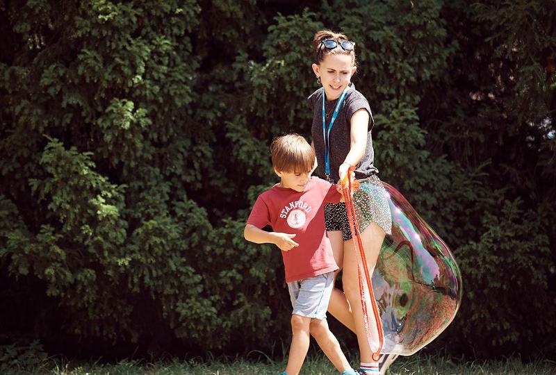 Eine Betreuerin im Ferienprogramm Villingen-Schwenningen hilft einem Campteilnehmer beim Seifenblasen machen