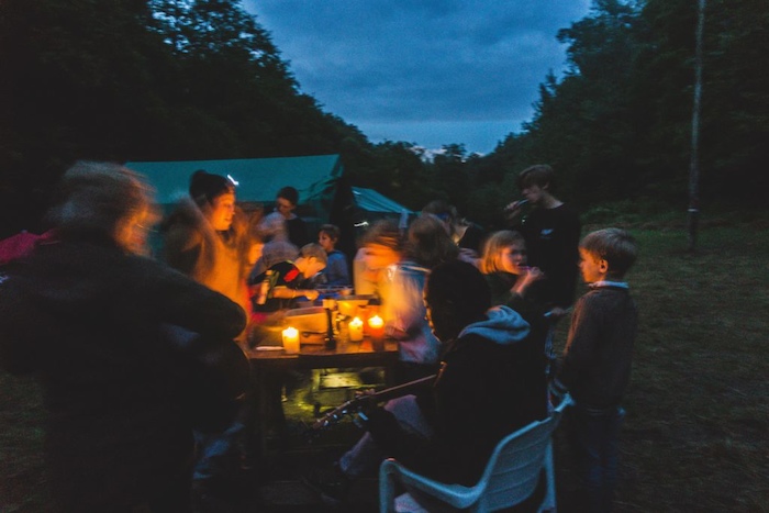 Kinderen en jongeren zitten 's avonds bij kaarslicht in het tentenkamp.