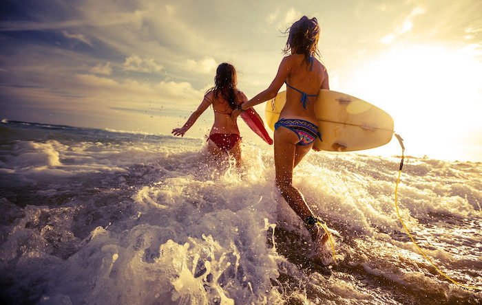 Twee tienermeisjes wandelen op surfkamp in Spanje in de golven met surfboards.