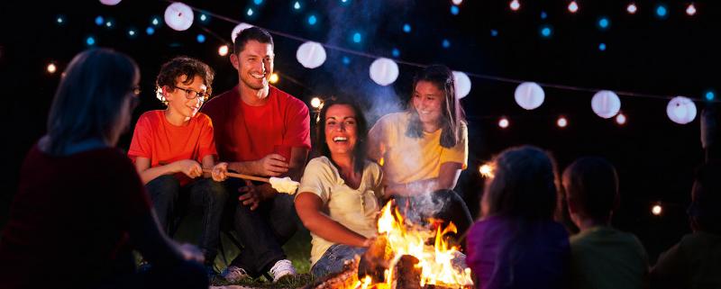 Eine Familie macht sich Stockbrot und sitzt gemeinsam beim Lagerfeuer