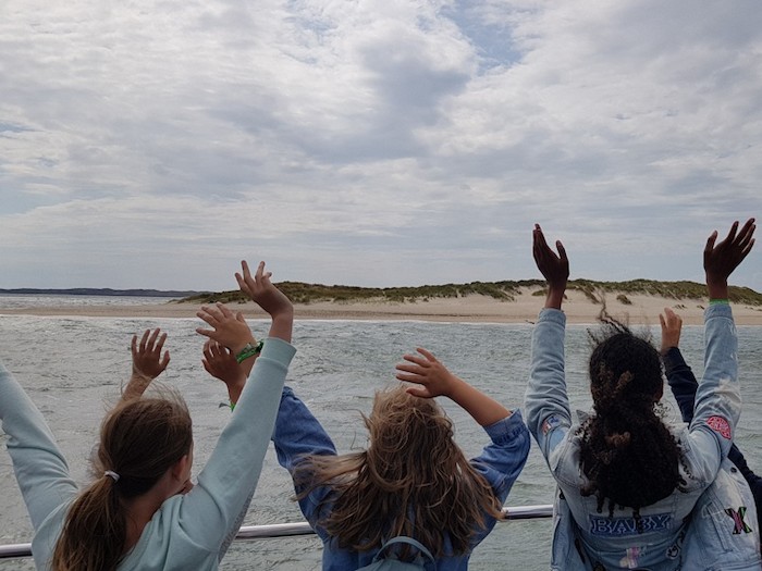 Drei Kinder stehen mit dem Rücken zur Kamera und schauen vom Wasser aus auf den Strand.