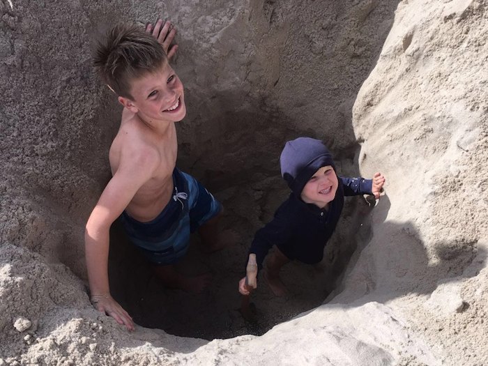 Zwei Jungs lächeln in ihrer selbstgegrabenen Sandgrube im Ferienlager auf Sylt