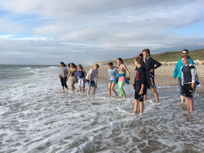 Kinder stehen mit den Füßen am Strand im Meer.