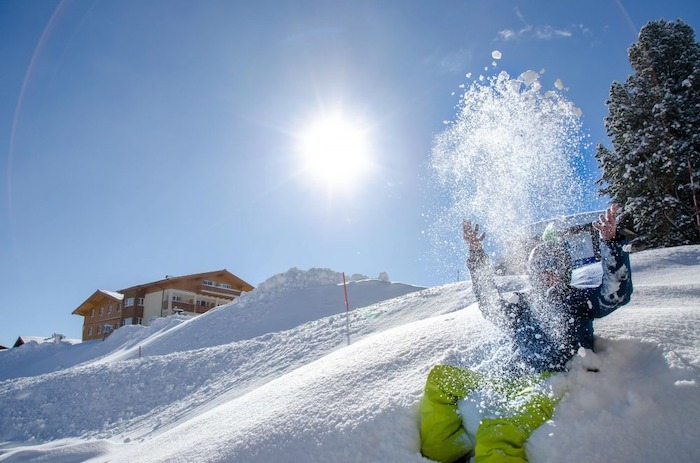 Jugendlicher wirft im Sonnenschein Schnee hoch auf der Skifreizeit Österreich