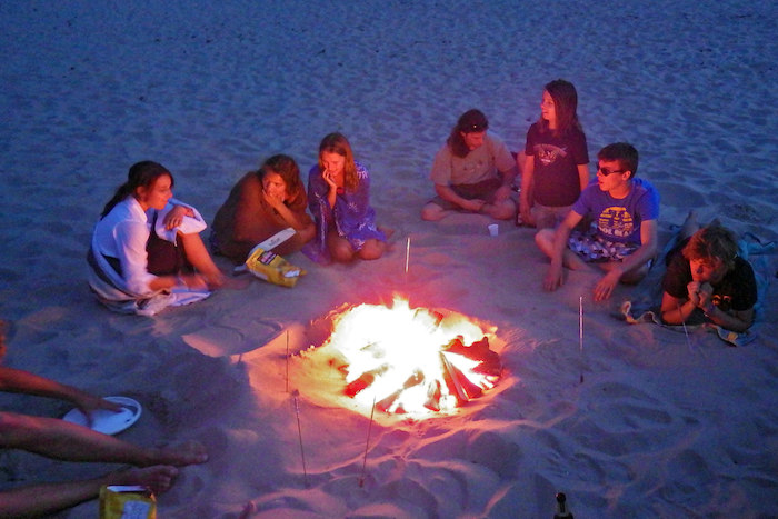 Jugendliche sitzen auf Jugendreise Surfen abends am Lagerfeuer
