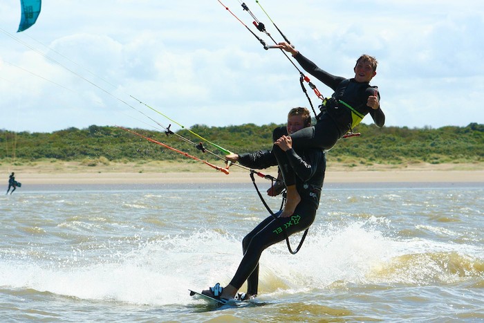 Ein Junge sitzt im Kitesurfcamp auf der Schulter eines anderen während sie kitesurfen