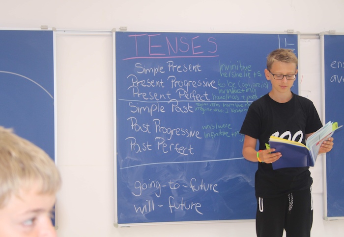 Junge steht vor einer blauen Tafel und hält einen Vortrag über englische Grammatik
