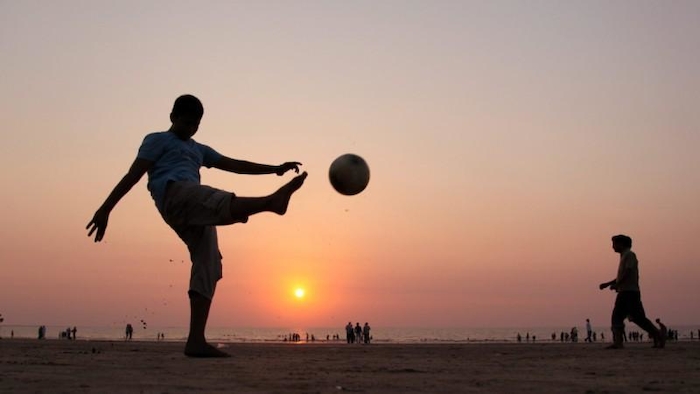 Ein Junge kickt einen Ball am Strand in den Sonnenuntergang im Fussballcamp.