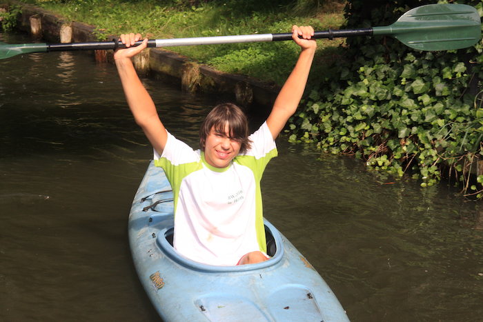 Junge hebt lächelnd Paddel hoch im Ferienlager im Spreewald