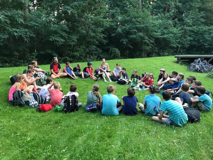 Kinder sitzen im Kreis auf der Wiese im Ferienlager im Spreewald