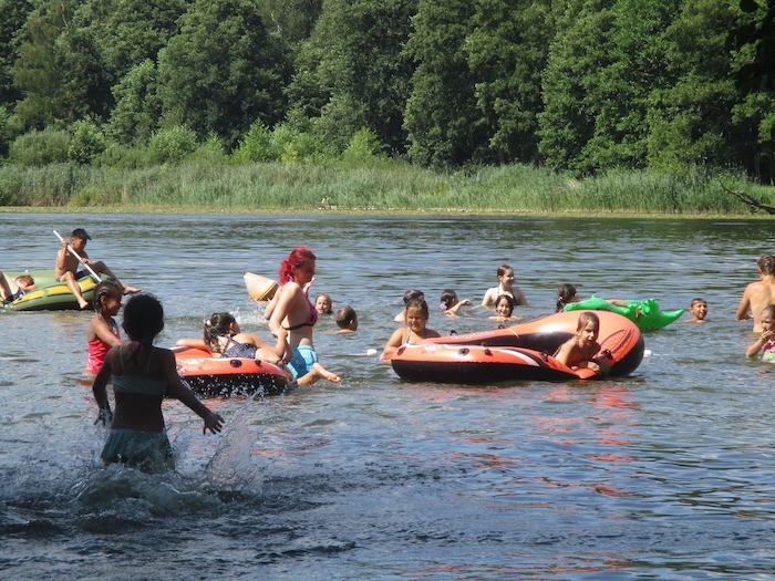 Kinder paddeln auf Schlauchbooten über den See im Ferienlager in Brandenburg