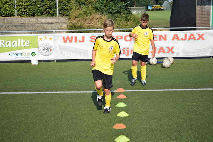 Jongen in geel shirt oefent dribbel op voetbalkamp