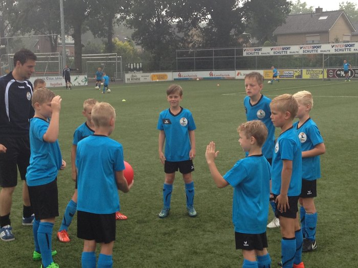 Jongens luisteren op voetbalkamp aandachtig naar trainer. 