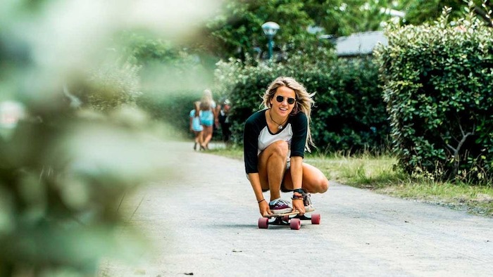 Geknield rijdt meisje met zonnebril op longboard.
