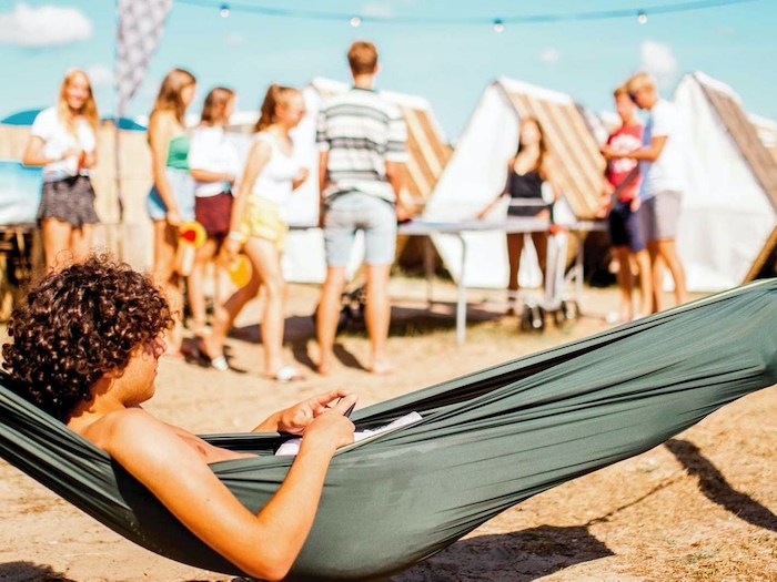 Jongen met krulhaar ligt in hangmat tijdens een zomerkamp jeugd