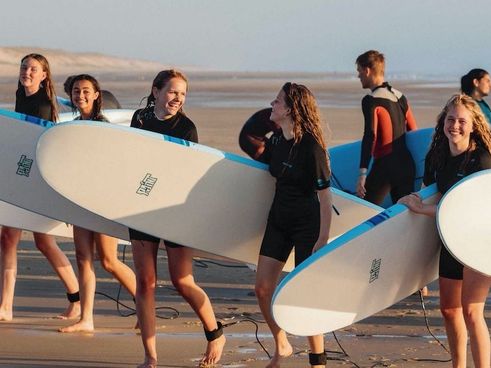 Meisjes wandelen op strand met surfboards tijdens kamp meivakantie.