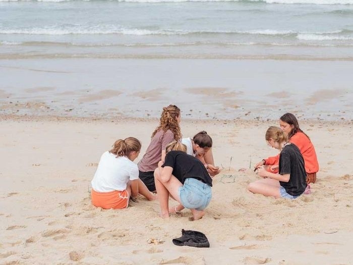Op kamp meivakantie zitten deelnemers in het zand en bouwen zandkasteel.