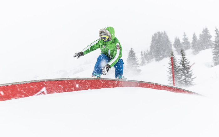 In der Skifreizeit rutscht ein Schüler grade über eine Stange mit dem Snowboard an den Füßen