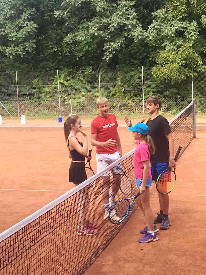 Kinder eines Sportcamps spielen Tennis
