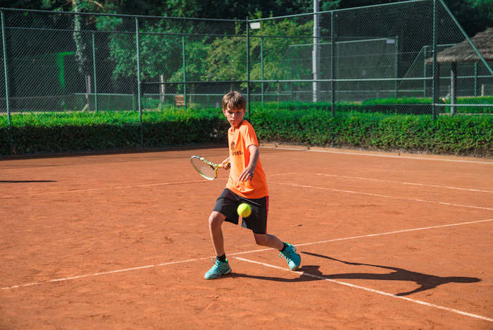 Ein Junge einer Kinderreise Holland schlägt beim Tennis einen Ball