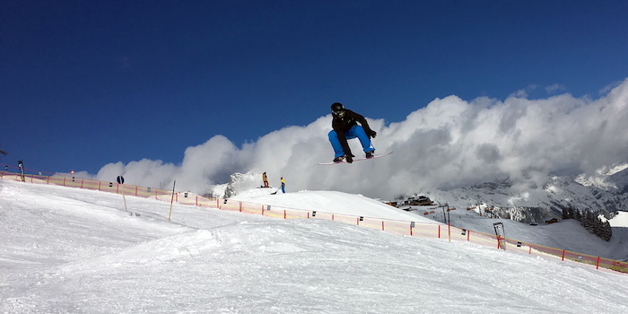 In den Winterferien in München springt ein Campteilnehmer mit seinem Snowboard über eine Schanze