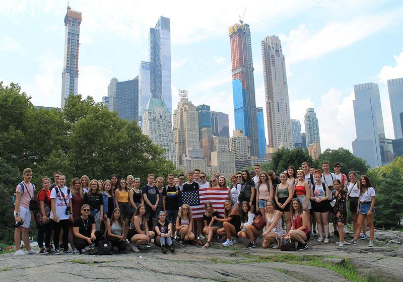 Eine große Gruppe von Kindern posiert in einer Reihe nebeneinander und halten die amerikanische Flagge bei unseren Sprachreisen USA für Schüler in Gastfamilie