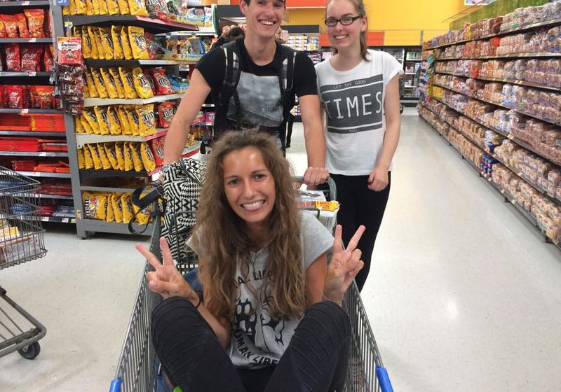 Drei Kinder haben Spass beim Shoppen, während eines der Mädchen im Einkaufswagen geschoben wird und das Peace Zeichen macht bei unseren Sprachreisen Amerika für Schüler