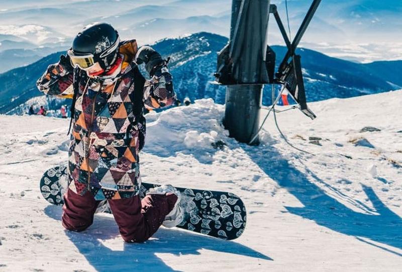 Teilnehmer einer Jugendreise ohne Eltern liegen mit dem Snowboard auf der Piste