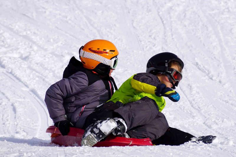 Zwei Kinder im Schnee auf einer Rodel auf Sprachferien Deutschland.