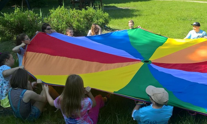 Teilnehmer eines Feriencamps für Kinder spielen Windtuch