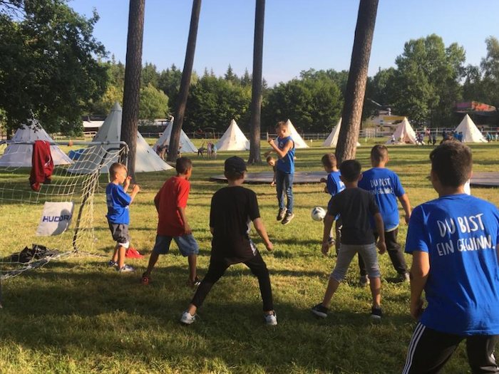 Einige Kinder spielen Fußball auf einer großen Wiese vor ihren Zelten und sie haben alle eine spaßige Zeit bei dem Zeltlager Pfingsten