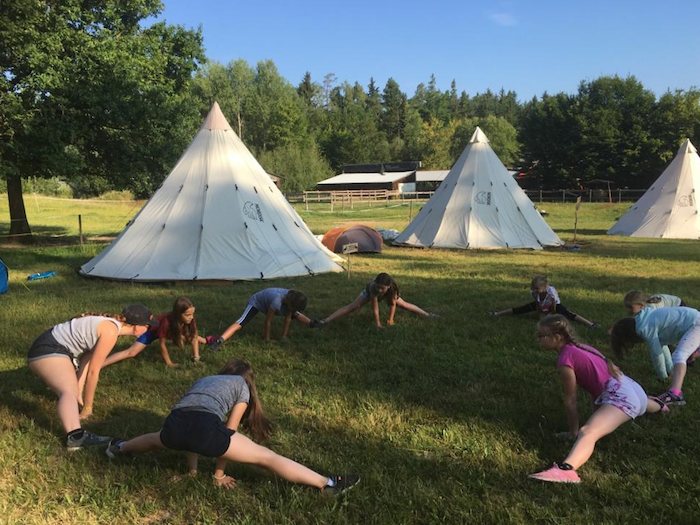 Einige Kinder machen am Morgen direkt vor ihren Zelten eine Yogaübung wo sie in den Spagat gehen bei dem Zeltlager Pfingsten