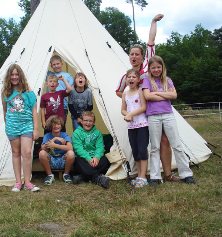 Einige Kinder posieren für ein Gruppenfoto vor einem sehr großen Zelt und genießen ihre Zeit bei dem Zeltlager Pfingsten